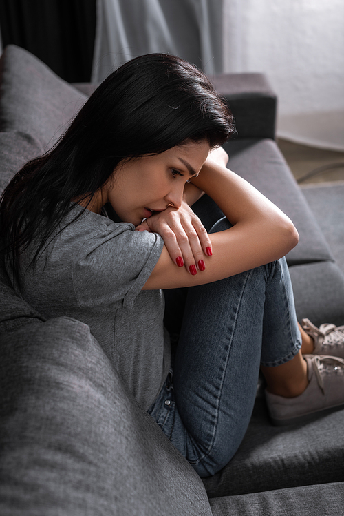 upset woman in jeans sitting on sofa, domestic violence concept