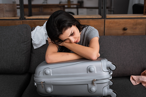depressed woman with bruise on face sitting on sofa near suitcase, domestic violence concept