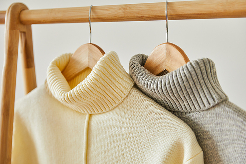 close up view of beige and grey knitted soft sweaters hanging on wooden hangers isolated on white