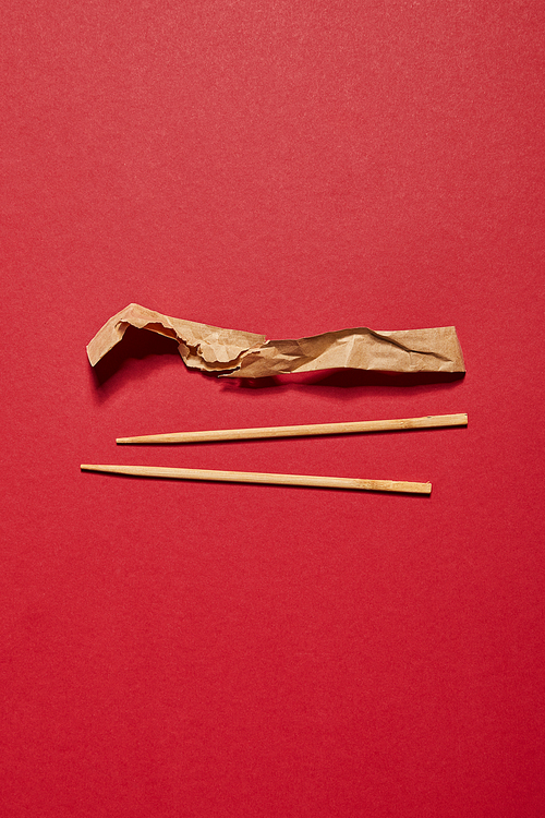 top view of wooden chopsticks near paper on red