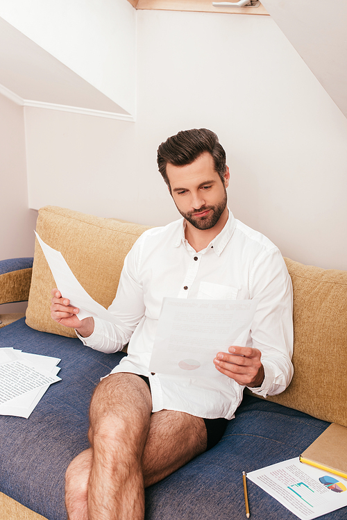 Handsome freelancer in panties and shirt working with papers near book on couch