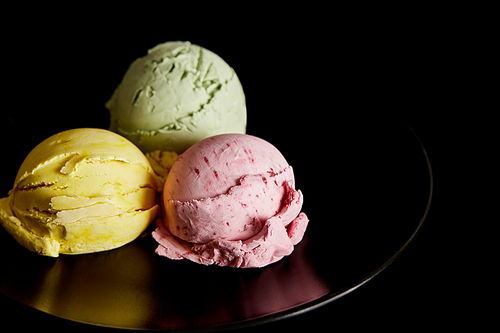 delicious yellow, pink and green ice cream balls on plate isolated on black