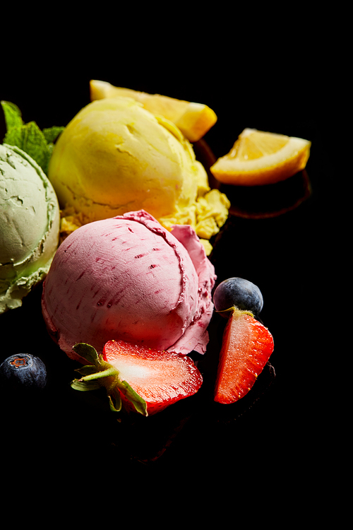 selective focus of delicious lemon, berry and mint ice cream balls isolated on black