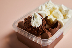 selective focus of tasty brown and white ice cream in plastic container on pink background