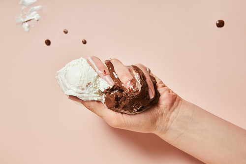 cropped view of woman holding melted brown and white ice cream on pink background