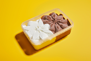 fresh tasty brown and white ice cream in container on yellow background