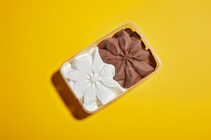 top view of fresh tasty brown and white ice cream in container on yellow background