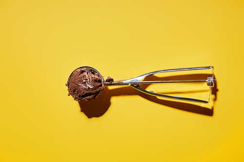 top view of fresh chocolate ice cream ball in scoop on yellow background