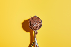 top view of fresh chocolate ice cream ball in scoop on yellow background