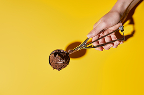 partial view of woman holding fresh chocolate ice cream ball in scoop on yellow background