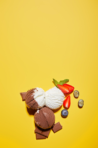 top view of tasty brown and white ice cream with berries, chocolate and mint on yellow background