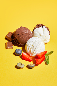 tasty brown and white ice cream with berries, chocolate and mint on yellow background