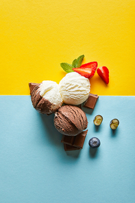 top view of tasty brown and white ice cream with berries, chocolate and mint on yellow and blue background