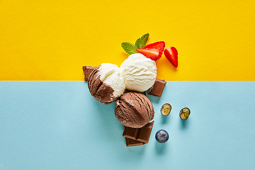 top view of tasty brown and white ice cream with berries, chocolate and mint on yellow and blue background