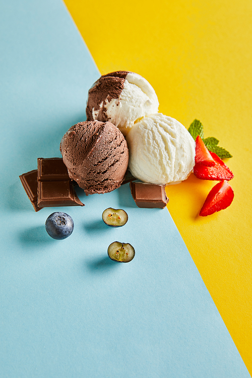 tasty brown and white ice cream with berries, chocolate and mint on blue and yellow background