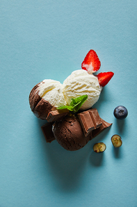 top view of tasty brown and white ice cream with berries, chocolate and mint on blue background