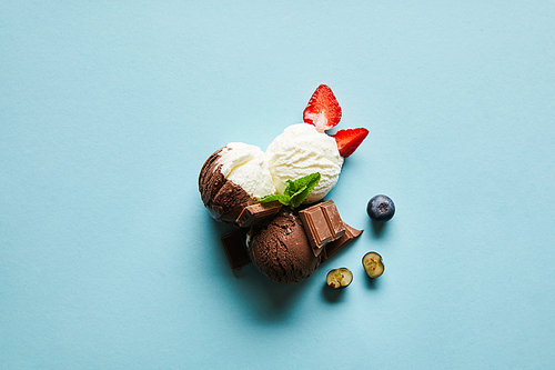 top view of tasty brown and white ice cream with berries, chocolate and mint on blue background