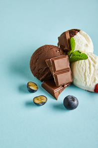 tasty brown and white ice cream with blueberries, chocolate and mint on blue background