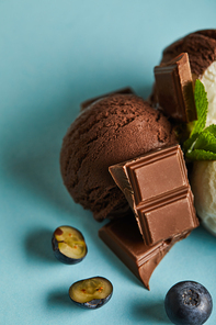 close up view of tasty brown ice cream with berries, chocolate and mint on blue background