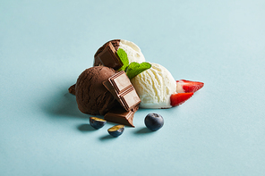 tasty brown and white ice cream with berries, chocolate and mint on blue background