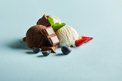 tasty brown and white ice cream with berries, chocolate and mint on blue background