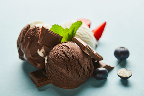 selective focus of tasty brown and white ice cream with berries, chocolate and mint on blue background