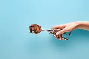 cropped view of woman holding scoop with chocolate ice cream on blue background