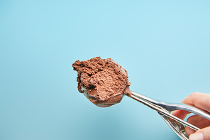 cropped view of woman holding scoop with chocolate ice cream on blue background