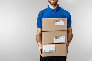 Cropped view of delivery man holding cardboard packages with qr codes and barcodes on cards isolated on grey