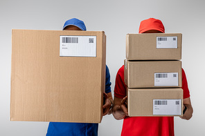 Delivery men holding cardboard packages with barcodes and qr codes on cards isolated on grey