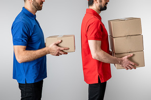 Side view of delivery men holding cardboard boxes isolated on grey