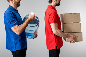 Side view of couriers holding cardboard boxes and bottled water isolated on grey