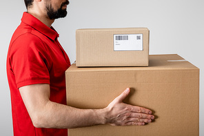 Side view of courier carrying cardboard boxes isolated on grey