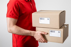 Cropped view of courier carrying cardboard packages with qr codes and barcodes on cards isolated on grey