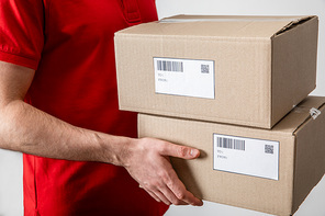 Cropped view of delivery man holding packages with qr codes and barcodes on cards isolated on grey