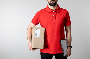 Cropped view of courier with clipboard and cardboard box isolated on grey