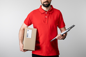 Cropped view of bearded courier holding clipboard and cardboard package isolated on grey