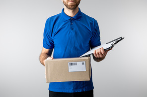 Cropped view of delivery man holding cardboard box and clipboard isolated on grey