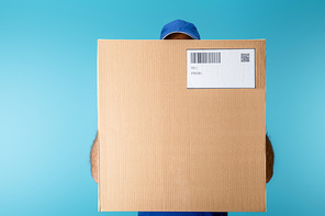 Courier holding cardboard box with qr and barcode isolated on blue