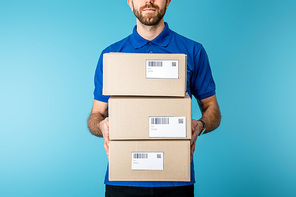 Cropped view of courier holding cardboard packages with qr codes and barcodes on cards isolated on blue