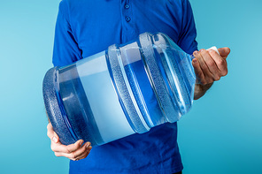 Cropped view of courier holding bottled water isolated on blue