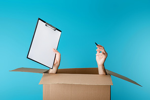 Hands of courier holding clipboard and pen from cardboard box isolated on blue