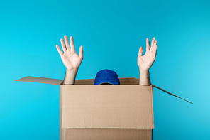 Hands and cap of delivery man in cardboard box isolated on blue