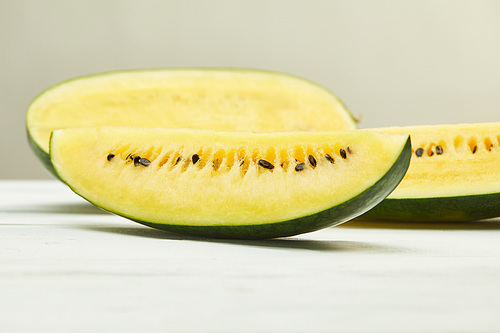 ripe yellow tasty watermelon with seeds on white wooden table isolated on grey