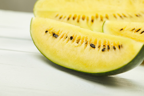 selective focus of ripe yellow tasty watermelon with seeds on white wooden table isolated on grey