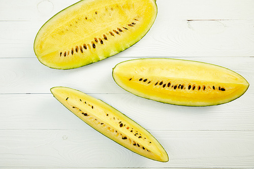 top view of ripe yellow tasty watermelon with seeds on white wooden table