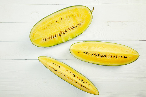 top view of ripe yellow watermelon with seeds on white wooden table