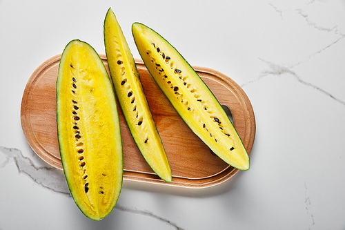 top view of cut delicious exotic yellow watermelon with seeds on wooden chopping board on marble surface