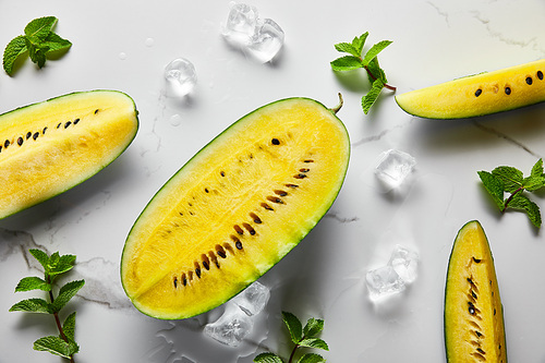top view of cut delicious exotic yellow watermelon with seeds on marble surface with mint, ice