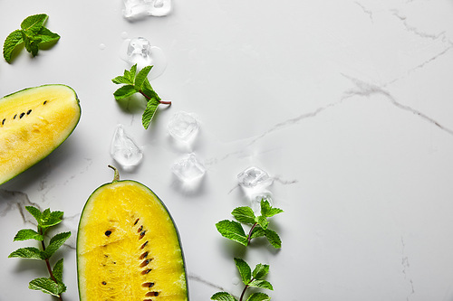 top view of cut delicious exotic yellow watermelon with seeds on marble surface with mint and ice